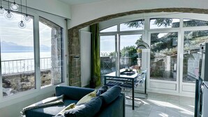 Una sala de estar moderna con un sofá azul, una mesa de comedor con sillas y ventanas grandes que ofrecen vista al mar.
