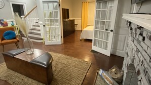 Una sala de estar con sofá, una mesa de centro y chimenea. Se ve una escalera que sube a otra habitación.