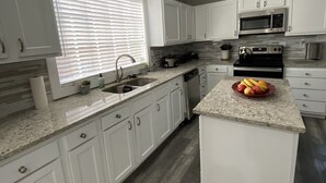 Una cocina moderna con armarios blancos, encimeras de granito y electrodomésticos de acero inoxidable.
