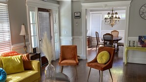 Una sala de estar amplia con un sofá amarillo, sillones naranjas, una mesa de centro de madera y una araña.
