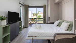 Habitación de hotel moderna con una cama grande, un televisor de pantalla plana, un estante verde y un balcón con mesa y sillas.