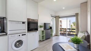 Cocina moderna con lavadora, horno y televisor integrado. Hay un comedor con mesa y sillas, y un balcón con vistas.