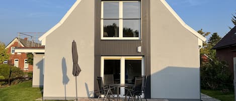 A modern two-story house with a patio, a dining table, and chairs.