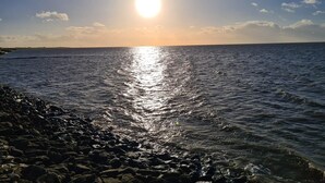Una playa con costa rocosa y mar tranquilo bajo un cielo despejado.
