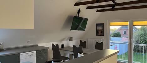 A modern kitchen with a dining area, a TV mounted on the wall, and a view of the outside.