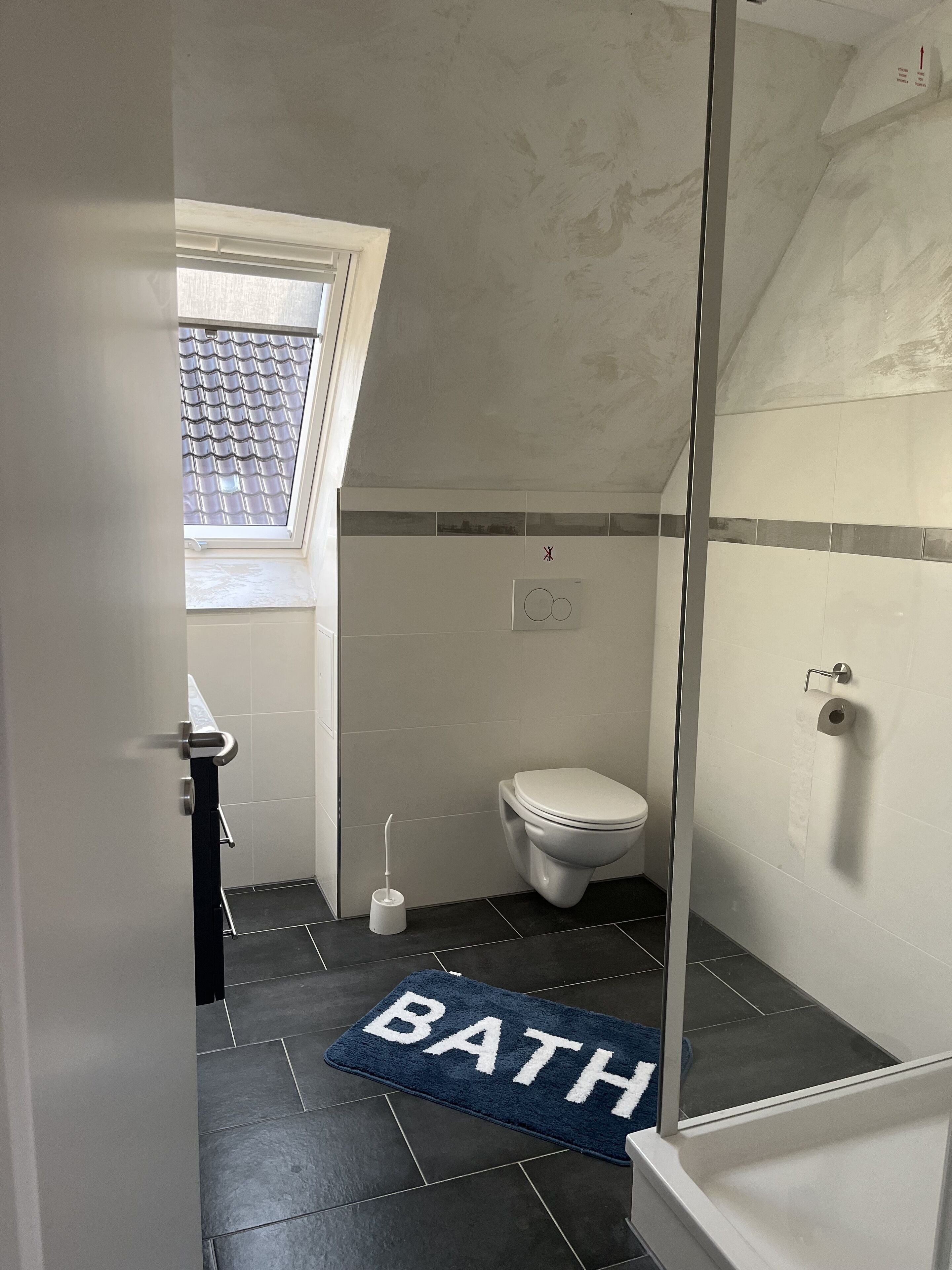 Une salle de bain avec des toilettes, une douche et une fenêtre.