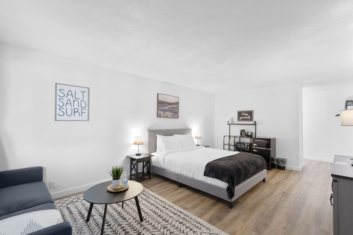 Um quarto moderno com cama, mesas de cabeceira, uma pequena mesa redonda, um sofá e uma parede com o letreiro 'Salt Sand Surf'.