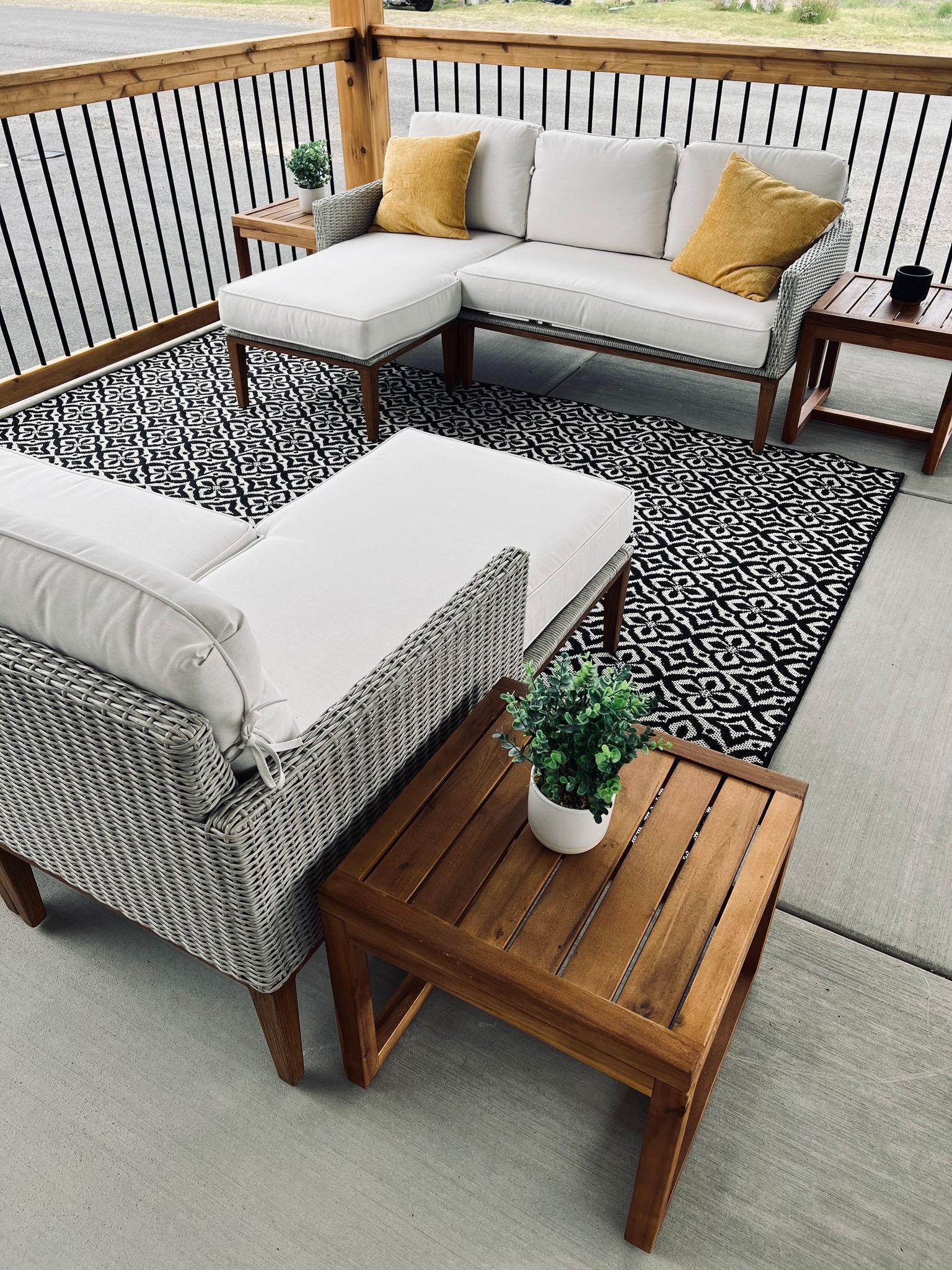 A covered outdoor seating area with a sectional sofa, a chaise lounge, and a wooden coffee table.