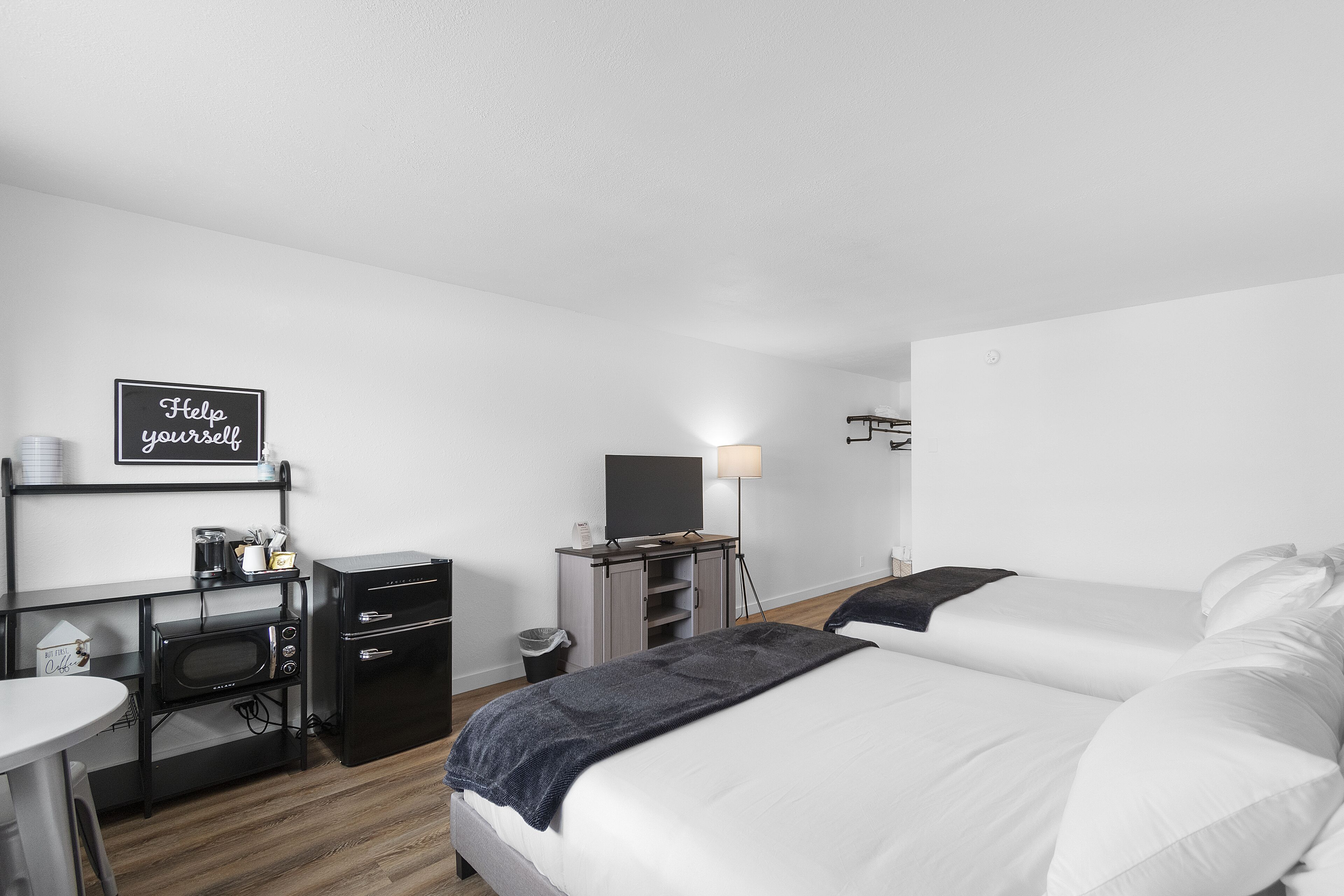 Moderni hotellihuone, jossa on sänky, työpöytä tietokoneella, mikroaaltouuni ja televisio.