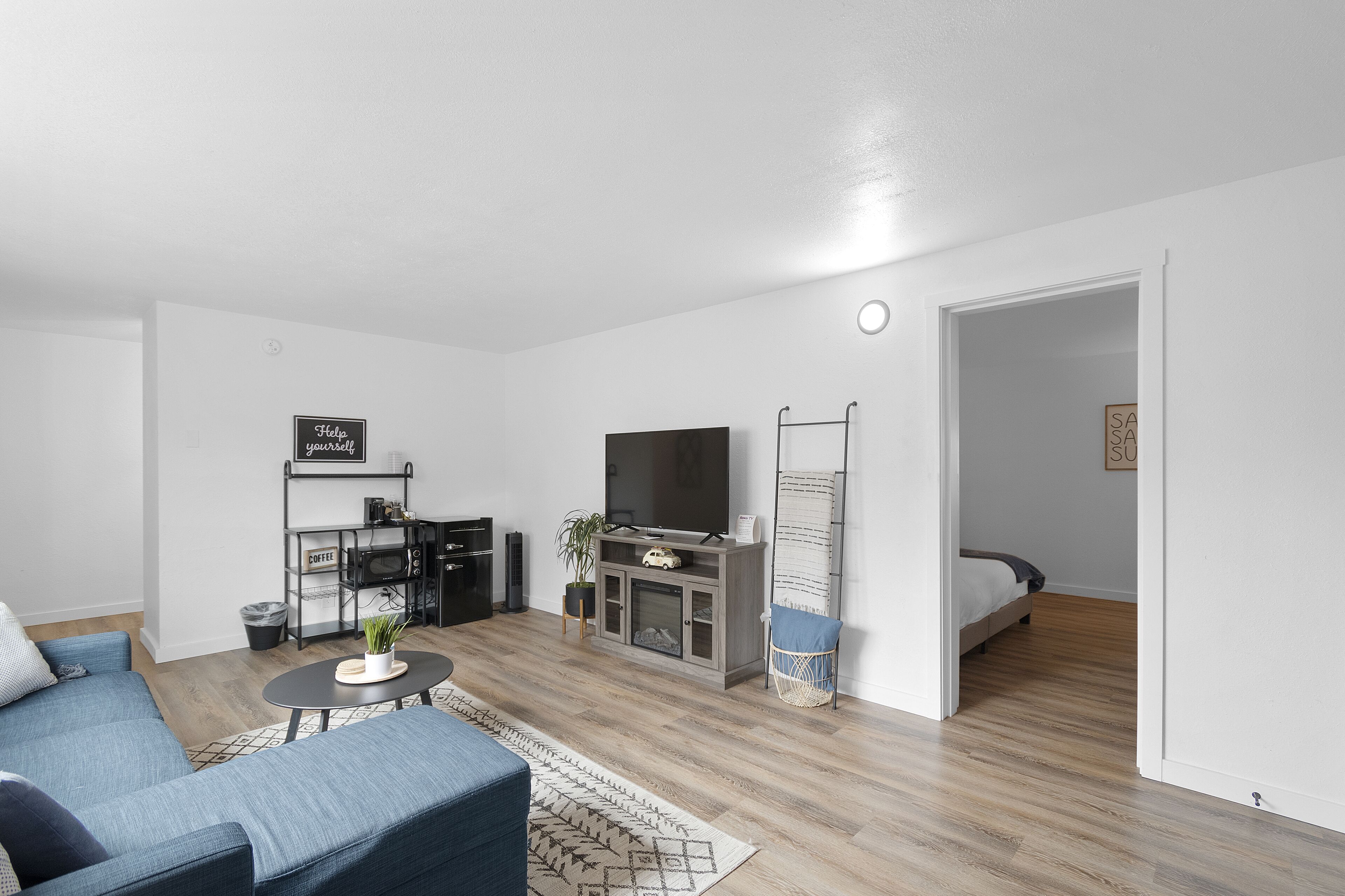 Una sala moderna con sofá, mesa de centro, televisor y una pequeña cocina.