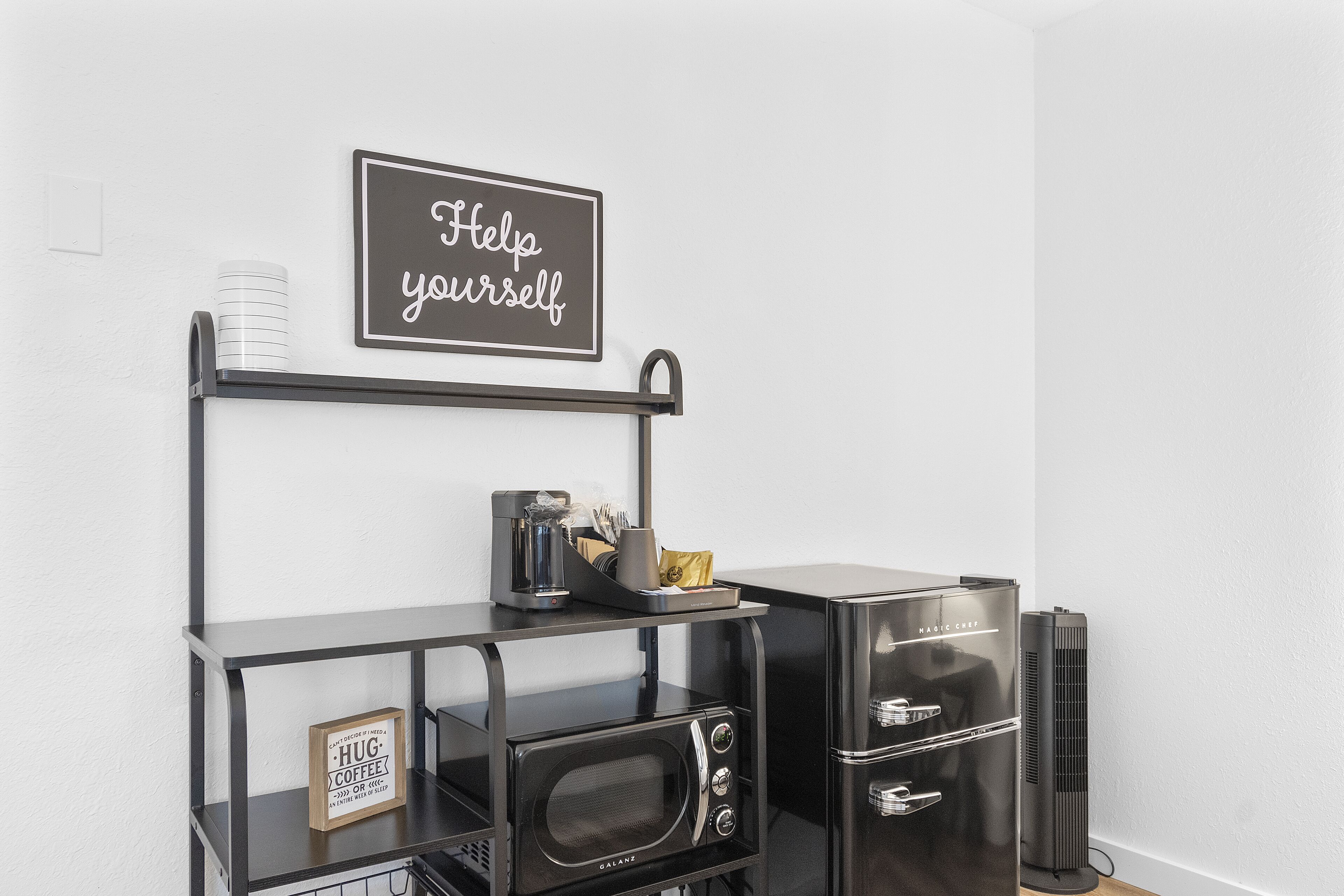 A kitchenette with a microwave, coffee maker, and a sign that says "Help yourself."