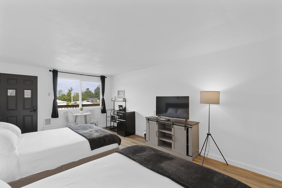 Quarto de hotel com duas camas, uma escrivaninha, uma televisão e um abajur.