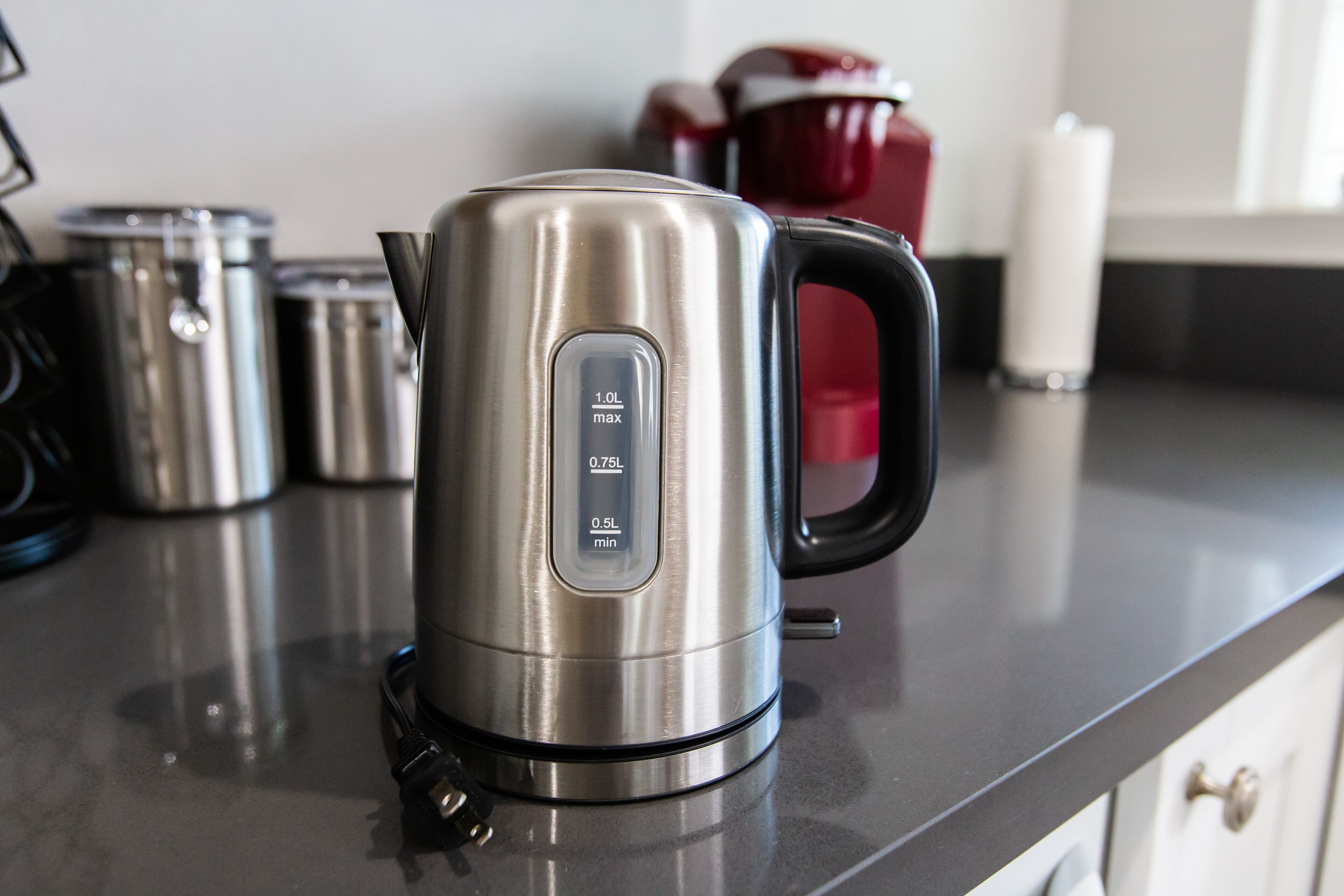 A stainless steel electric kettle on a kitchen countertop with a digital display showing 1.0L max, 0.75L, and 0.5L min settings.