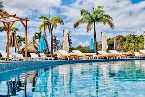 A pool area with lounge chairs and umbrellas, surrounded by palm trees. - Set in a lush green area, your bungalow is a few steps from a natural beach. (Grand-Bourg)