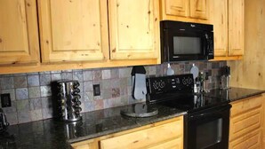 Une cuisine avec des meubles de rangement en bois, un micro-ondes noir, une cuisinière et une machine à café.