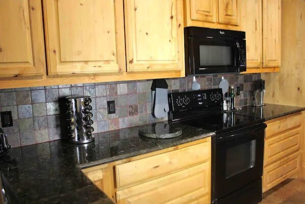 A kitchen with wooden cabinets, a black microwave, a stove, and a coffee maker.