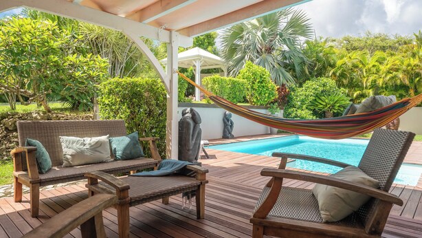 Une terrasse en bois avec un hamac, une piscine et une végétation luxuriante.