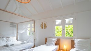 Une chambre avec deux lits en bois, une moustiquaire, une lampe de chevet et une fenêtre donnant sur un paysage verdoyant.