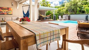 Une terrasse en bois avec une table et des chaises, un hamac et une piscine en arrière-plan.