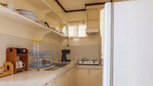 Eine kleine Küche mit weißen Schränken, einem weißen Kühlschrank, einer Kaffeemaschine und einem Spülbecken.