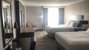 Een hotelkamer met een bed, een bureau, een stoel, een lamp en een groot raam met gordijnen.