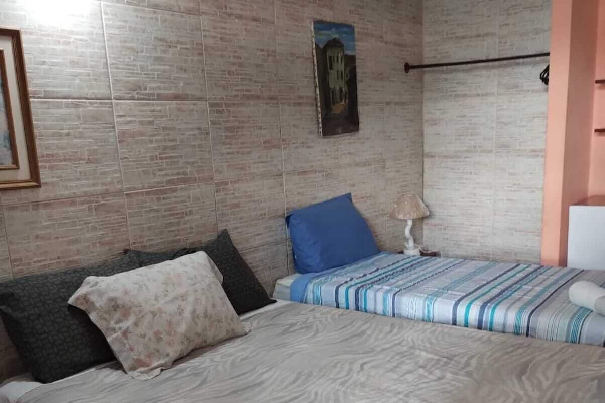 A bedroom with two beds, one with a striped bedspread and the other with a floral one. There are towels on the bed and a lamp on the side.