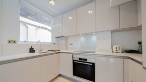 Une cuisine moderne avec des meubles blancs, un four encastré, un évier et une fenêtre.