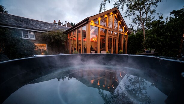 A hot tub with a wooden deck and glass walls, surrounded by trees and a house in the background. - Oakhouse - sleeps 16 guests  in 5 bedrooms (Preston)