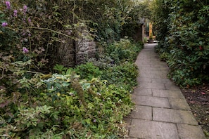 Stroll through lush gardens to a traditional building with a sloped roof.