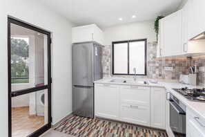 A modern kitchen with white cabinets, a stainless steel refrigerator, a window with a patterned view, and a tiled backsplash.
