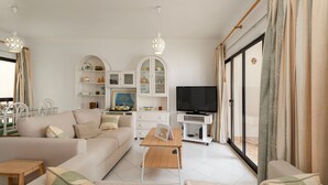 Uma sala de estar moderna com sofá, mesa de centro e aparador para TV. Há armários com objetos decorativos e uma porta de vidro deslizante.