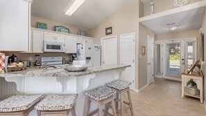 Una cocina con armarios blancos, encimera de granito y una isla central con taburetes.