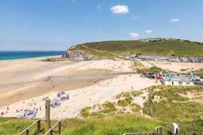 A beach with a sandy shore, a grassy hill, and a building with flags.