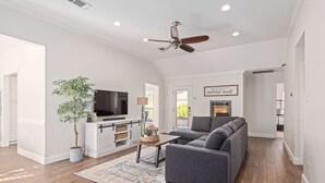 A spacious living room with a grey sofa, a flat-screen TV, a ceiling fan, and a potted plant. - Home Pool 15 Minutes from DFW Airport (Flower Mound)