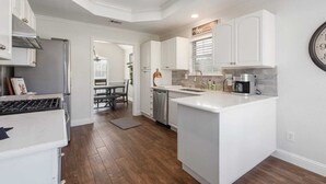 A modern kitchen with white cabinetry, a central island, and a dining area with a table and chairs. - Home Pool 15 Minutes from DFW Airport (Flower Mound)