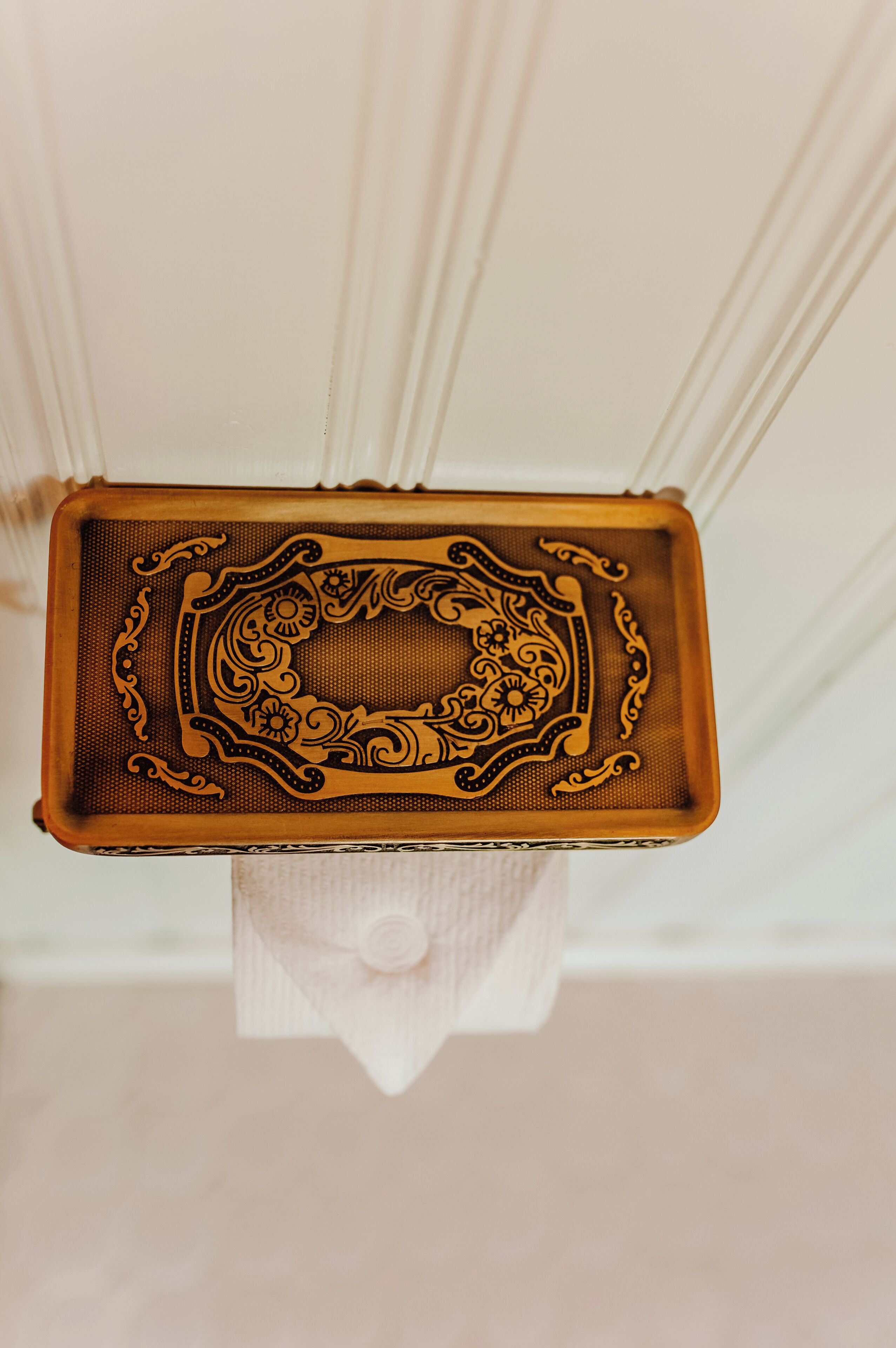 Un plateau rectangulaire orné de motifs floraux complexes et doté d’un bouton central, posé sur un support blanc.