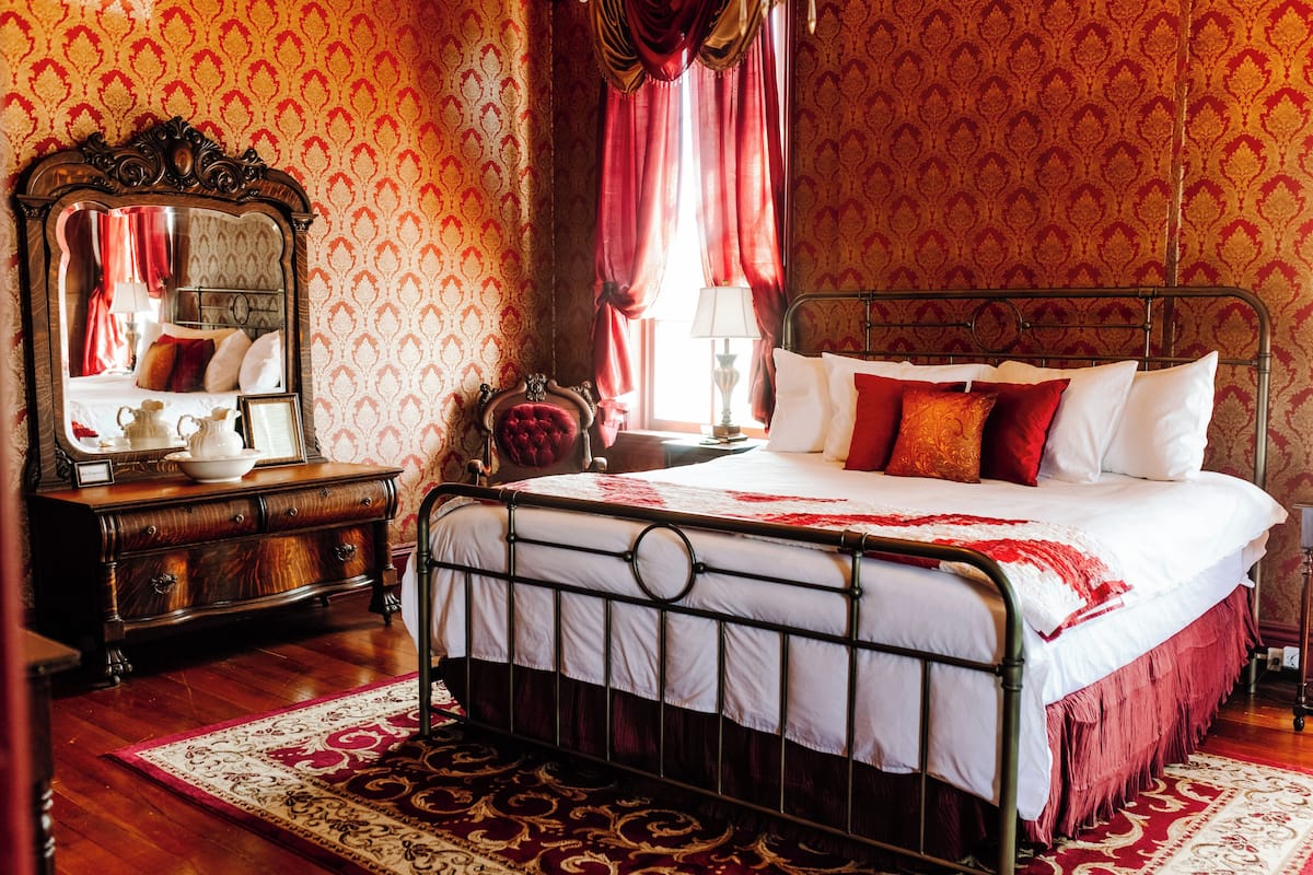 Ein traditionell eingerichtetes Schlafzimmer mit einem Himmelbett, einer Holzkommode und einem großen Spiegel.