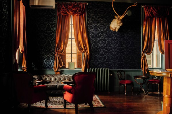 Une pièce avec un canapé en cuir, des fauteuils rouges, une table et une tête d’animal fixée au mur.