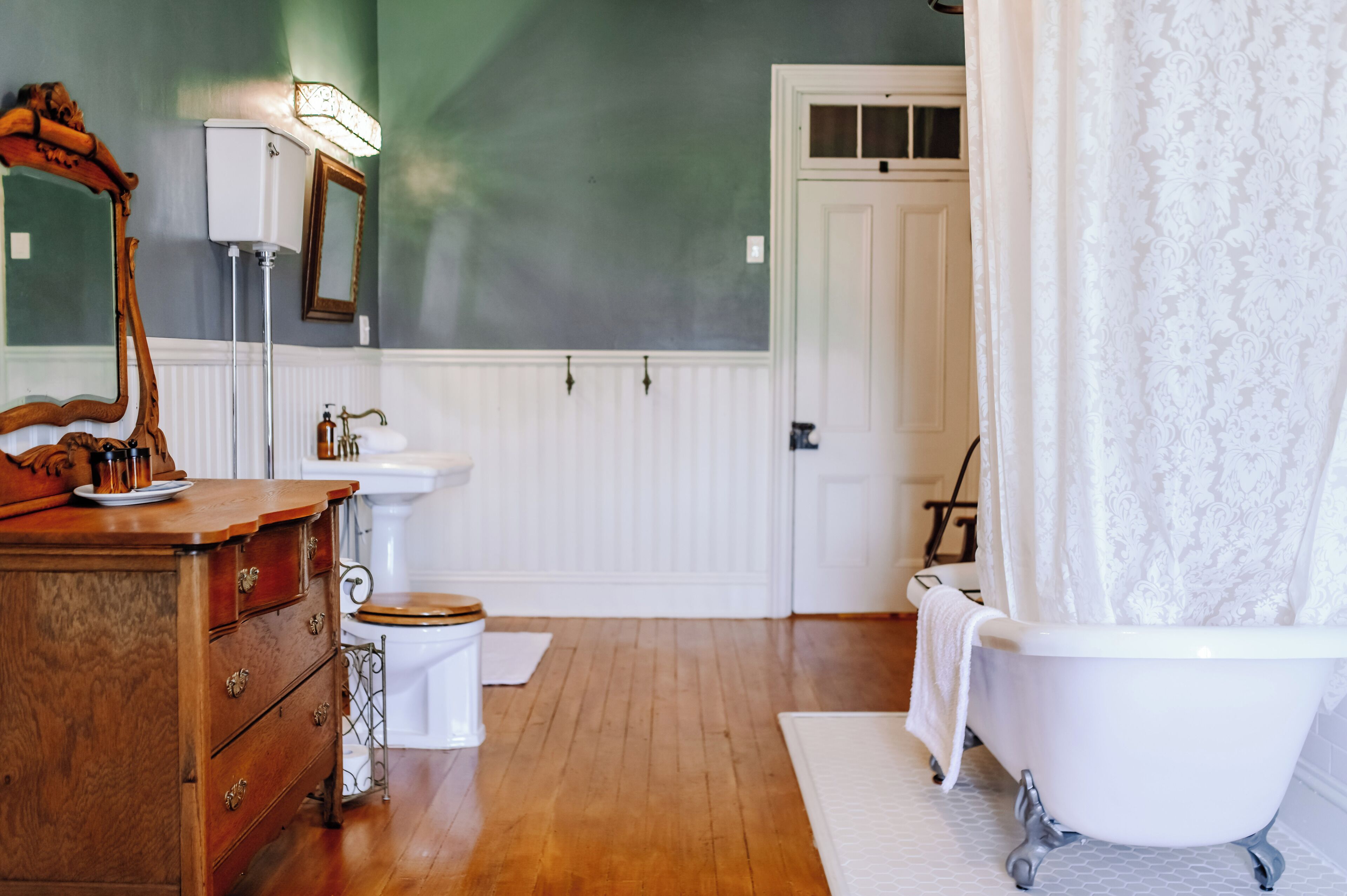 Une salle de bain avec une commode en bois, un lavabo blanc et une baignoire sur pieds.