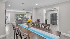 A modern dining area with a long table, chairs, and a vase of yellow flowers.