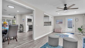A modern kitchen with white cabinets, a microwave, and a stove. There is a dining area with a table and chairs, and a ceiling fan above.