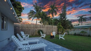 A backyard patio with white Adirondack chairs, a fire pit, and a wooden fence.