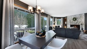 A modern living room with a dark wooden dining table, white chairs, and a stone fireplace.