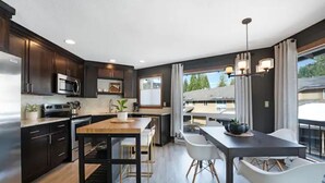 A modern kitchen with dark cabinetry, stainless steel appliances, a wooden dining table, and white chairs.