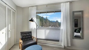A room with a large window, a chair, a floor lamp, and a mirror on the wall.
