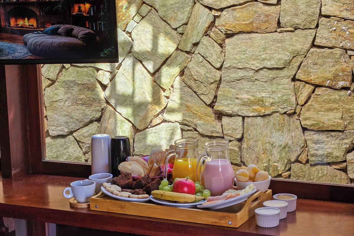A breakfast tray with various foods and drinks, a stone wall, and a television in the background.
