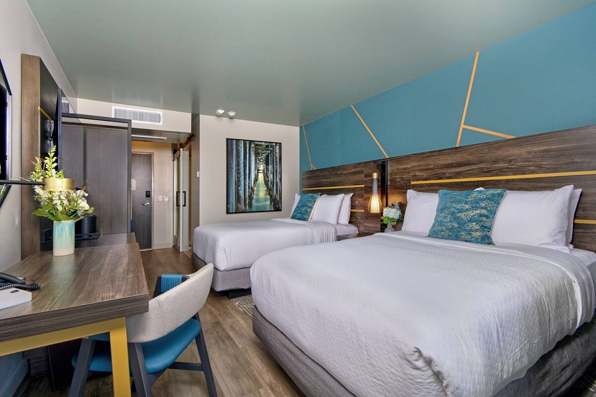 A hotel room with two beds, a desk, and a chair.