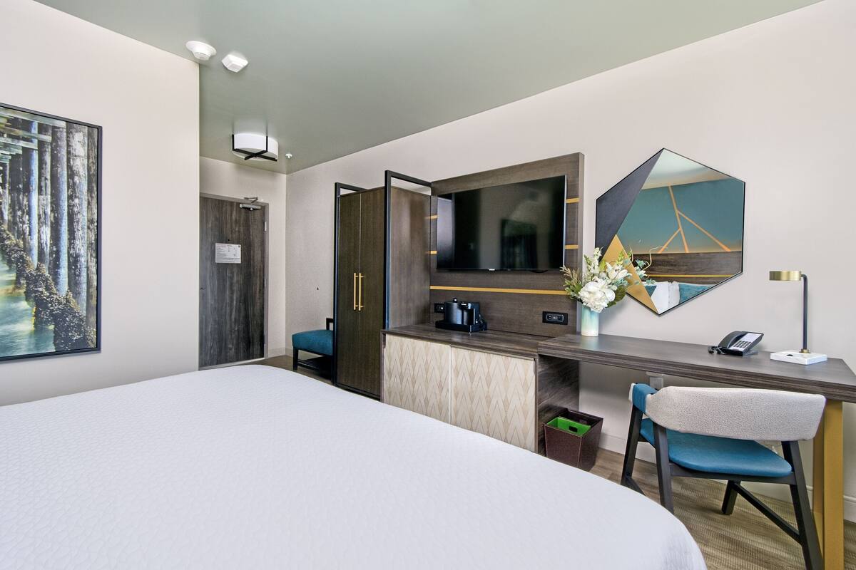 A hotel room with a large bed, a desk with a chair, a coffee maker, a telephone, and a mirror.