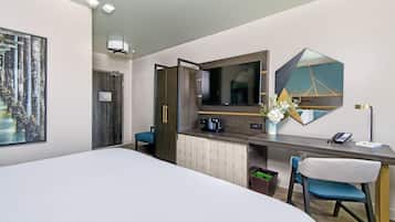 Habitación de hotel con una cama grande, un escritorio con una silla, una cafetera, un teléfono y un espejo.
