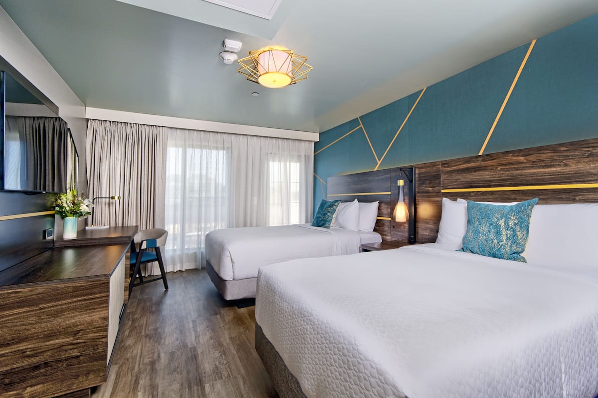 A hotel room with two beds, a desk, and a TV.